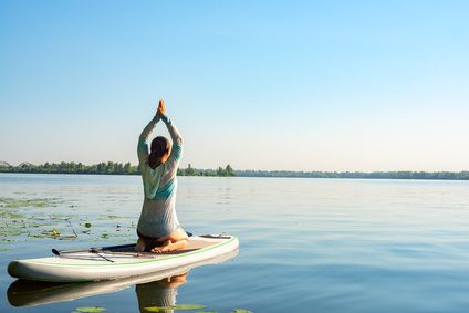 SUP-Yoga: Teilnehmerin im Fersensitz auf dem Board, Arme über dem Kopf