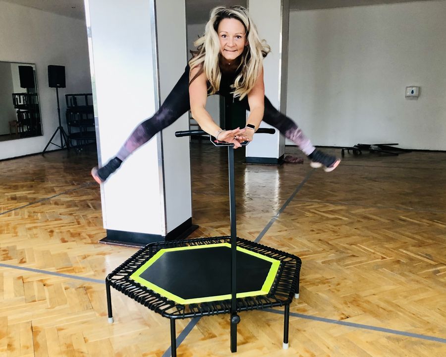 Trainerin springt lachend auf einem Mini-Trampolin im hellen Kursraum